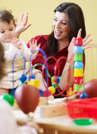 Child care provider engaging with a baby and two toddlers in a hands-on learning activity